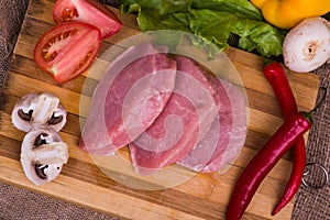 Sliced pieces of raw meat for barbecue with fresh Vegetables tomatoes, lettuce on wooden surface. Top view.