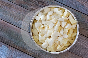 Sliced pieces of raw potatoes in a circular bowl on an old rustic wooden table