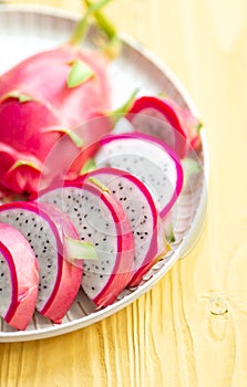 Sliced pink dragon fruit in plate on yellow wood background