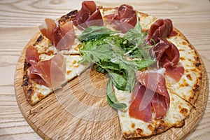 Sliced pizza with parma ham, salad rocket and parmesan on wooden