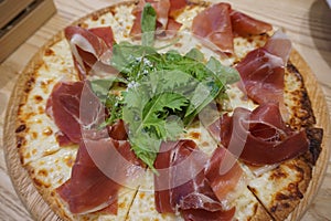 Sliced pizza with parma ham, salad rocket and parmesan on wooden