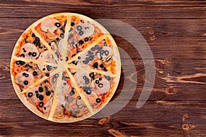 Sliced pizza wwith ham, mozzarella, mushrooms and olives on round wood platter which is on wooden rustic background, top view