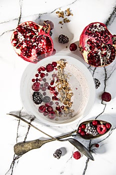 Sliced pomegranate and homemade fresh yoghurt with forest fruits and cereal. White marble pattern background.