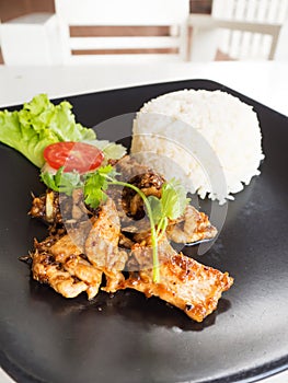 Sliced pork fried served with rice. On black plate.