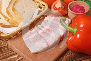 Sliced pork jowl bacon closeup with bread, pepper, tomatoes and horseradish sauce photo