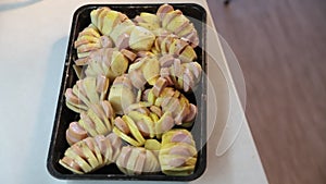 Sliced potatoes with sausages on a baking sheet are sprinkled with spices.
