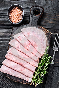 Sliced prosciutto ham on wooden cutting board. Black wooden background. Top view