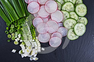 Sliced radish, Cucumber, Green onion on the black slate board. Ingredients for vitamin spring salad