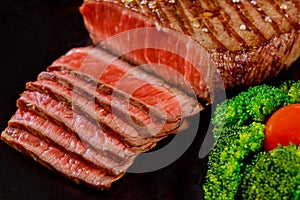 Sliced rare beef tenderloin with broccoli on black background