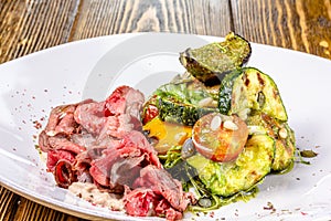 Sliced rare roast sirloin of beef with roasted vegetables on rustic wooden background