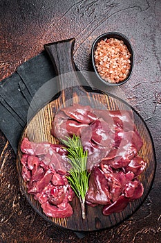 Sliced Raw chicken liver, fresh fowl offals on wooden board. Dark background. Top view
