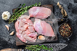 Sliced Raw Chicken thigh fillet on a wooden cutting board. Black background. Top view