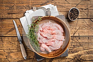 Sliced raw chicken, turkey breast meat in a wooden plate with thyme. Wooden background. Top view