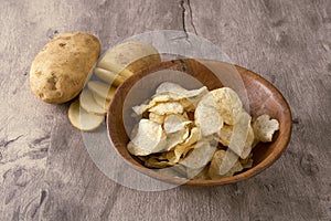 Sliced raw potato and potato chips on a wooden bowl over wood background