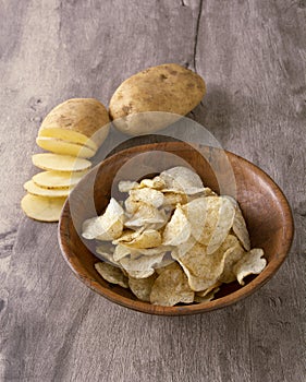 Sliced raw potato and potato chips on a wooden bowl over wood background