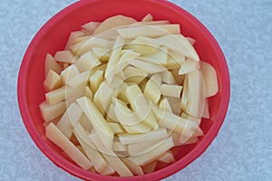 Sliced raw potatoes in a red plastic plate. Outdoor