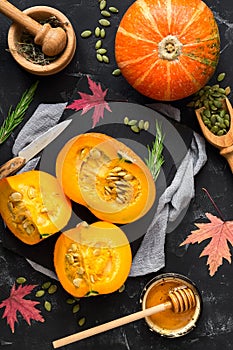 Sliced raw pumpkin with herbs, seeds and honey on a black stone background. Autumn food background. Thanksgiving and halloween
