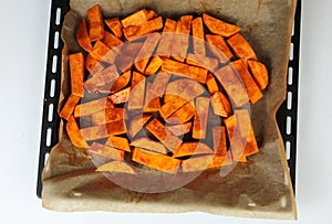 Sliced raw sweet potato with oil and spices on the baking paper, oven pan