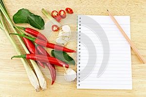 Sliced red hot chili pepper with bergamot leaves, garlic, galangal and lemon grass and notebook with pencil