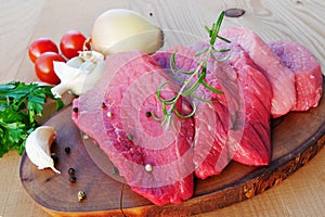 Sliced red meat on wooden board with herbs and spices