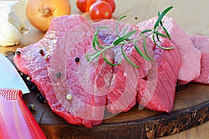 Sliced red meat on wooden board with herbs and spices