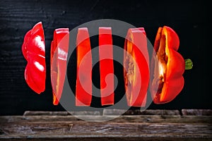 Sliced red pepper on the fly over wooden table.