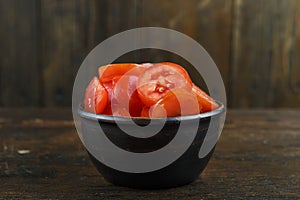 Sliced red tomato in a bowl on a wooden background. Vegetable, ingredient and staple food