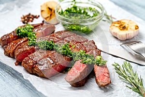 Sliced rib eye beef steak with chimichurri sauce and spices on white paper. Striploin cooked on the grill