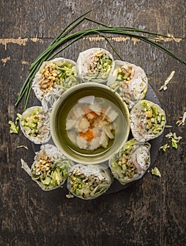Sliced rice rolls lined circle around a bowl of vegetable soup on wooden background top view