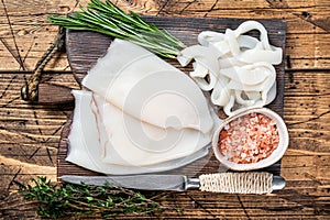 Sliced rings Raw Calamari or Squid on a wooden board with rosemary. wooden background. Top view