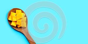 Sliced ripe mango cubes on wooden spoon on blue background