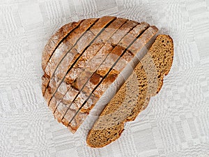 Sliced round loaf of rye bread with an appetizing crispy brown crust on a gray linen tablecloth. Tasty, usefull and nutritious.