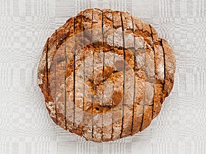 Sliced round loaf of rye bread with an appetizing crispy brown crust on a gray linen tablecloth. Tasty, usefull and nutritious.