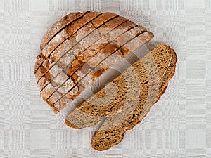 Sliced round loaf of rye bread with an appetizing crispy brown crust on a gray linen tablecloth. Tasty, usefull and nutritious.