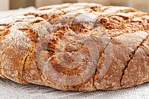 Sliced round loaf of rye bread with an appetizing crispy brown crust on a gray linen tablecloth. Tasty, usefull and nutritious.