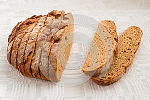 Sliced round loaf of rye bread with an appetizing crispy brown crust on a gray linen tablecloth. Tasty, usefull and nutritious.