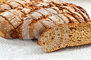 Sliced round loaf of rye bread with an appetizing crispy brown crust on a gray linen tablecloth. Tasty, usefull and nutritious.