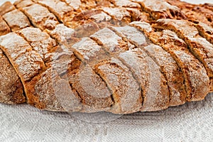 Sliced round loaf of rye bread with an appetizing crispy brown crust on a gray linen tablecloth. Tasty, usefull and nutritious.