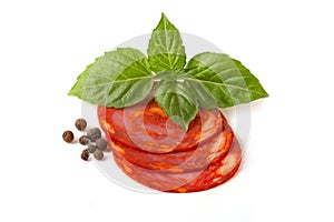 Sliced round pieces of raw-cured Chorizo sausage with basil leaf and pepper peas on a white background photo