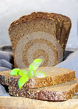 Sliced rye bread with leaf basil on cutting board. Whole grain rye bread with seeds