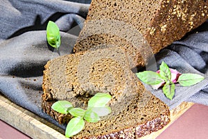 Sliced rye bread with leaf basil on cutting board. Whole grain rye bread with seeds