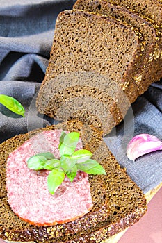 Sliced rye bread with leaf basil on cutting board. Whole grain rye bread with seeds