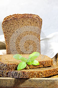 Sliced rye bread with leaf basil on cutting board. Whole grain rye bread with seeds