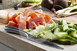 Sliced salad, tomato, cucumber and spring onion, on a wooden chopping board