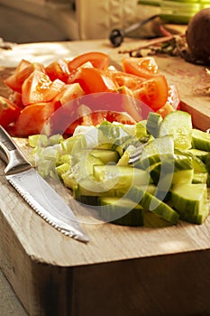Sliced salad, tomato, cucumber and spring onion, on a wooden chopping board with a knife