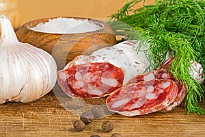 Sliced salame on cutting board, with dill, pepper, salt photo