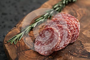 Sliced salame milano sausage on olive wood board with rosemary
