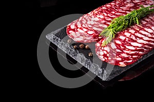 Sliced salami with dill and dry pepper on a slate serving Board. Black isolated background