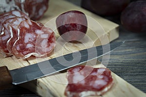 Sliced salami and grapes on wooden cutting board