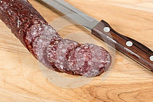 Sliced salami sausage and knife on wooden board